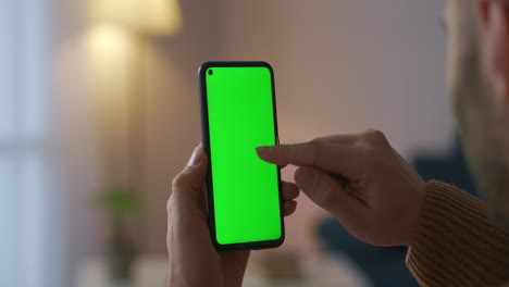 closeup-view-of-green-screen-of-modern-cell-phone-in-hands-of-male-user-scrolling-display-browsing-site-or-app-modern-technology